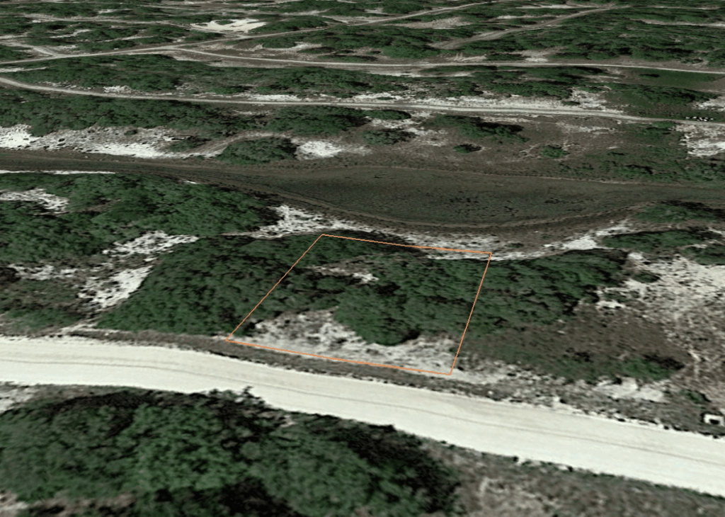 Aerial view of a small rectangular plot outlined in orange among shrubs and sandy ground beside a light-colored road.