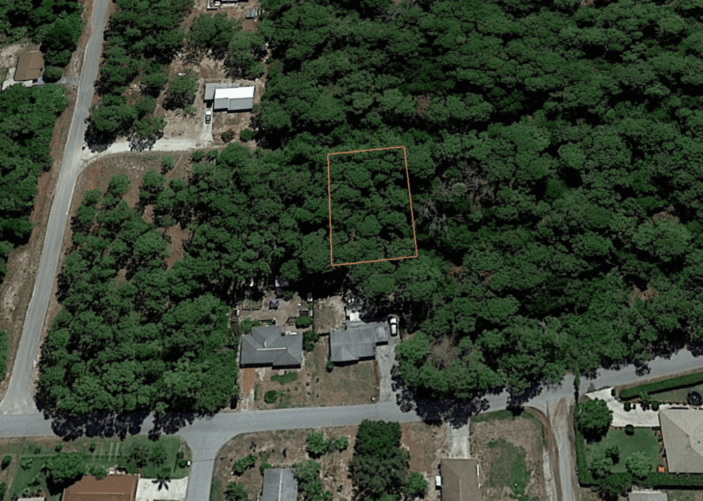 Aerial view of a wooded residential area with a rectangular lot outlined in orange among trees and houses nearby.