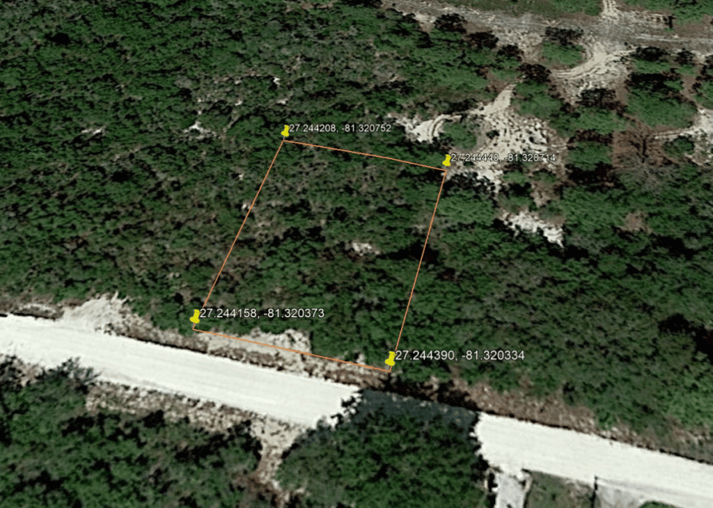 A wooded area with a small orange-outlined parcel and yellow pins at its corners, next to a white road; corner coordinates shown nearby (GPS).