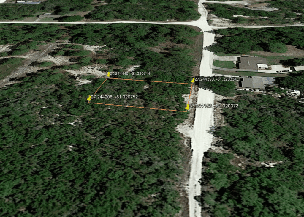 Aerial view of a rectangular wooded lot outlined in orange with four corner markers, beside a road and houses.