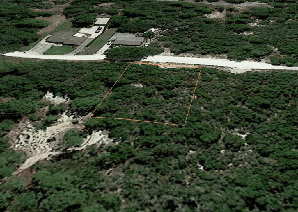 Aerial view of a wooded rectangular lot outlined in orange along a residential street, with nearby houses nearby vielseit?