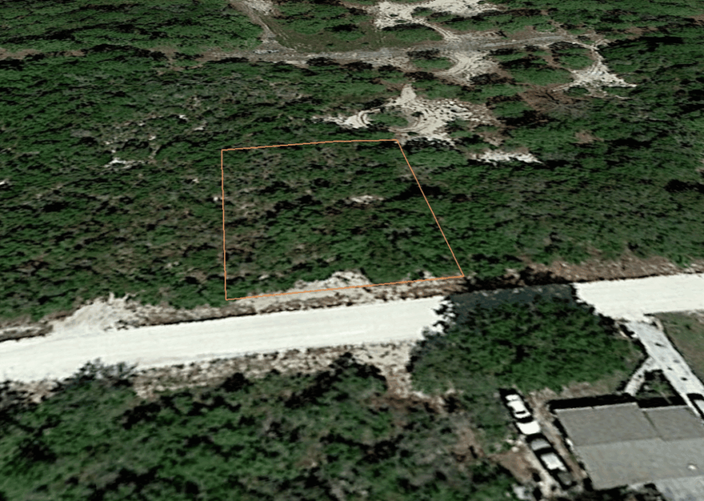 Aerial view of a rectangular vacant lot outlined in orange, bordered by a road and dense vegetation nearby.