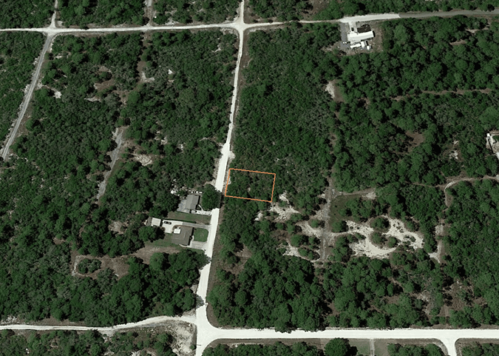 Aerial view of a forested area with grid roads; a rectangular lot is outlined in orange along a road.