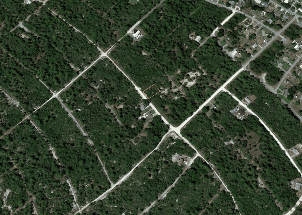 Aerial view of a wooded residential area with crisscrossing dirt roads and scattered houses; a small rectangular property is outlined in red.