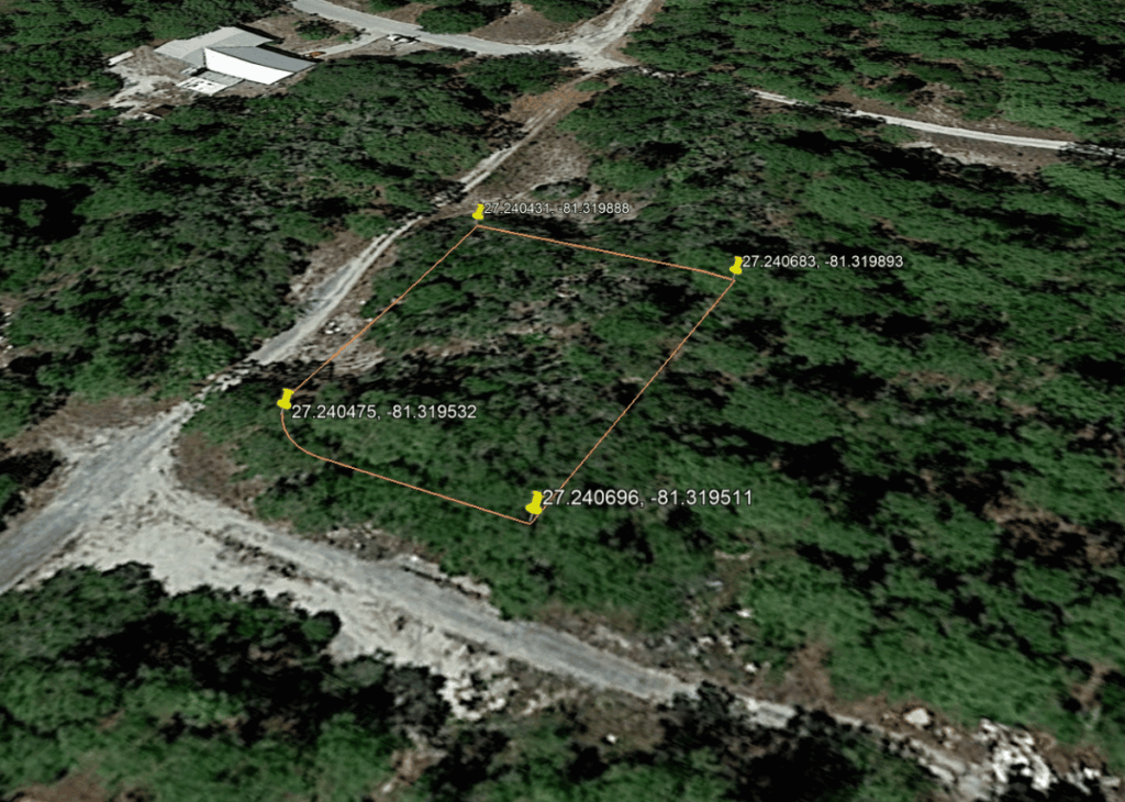 Aerial view of a forested site with an orange parcel boundary marked by four GPS pins and coordinates, near dirt roads and a building at the top-left.