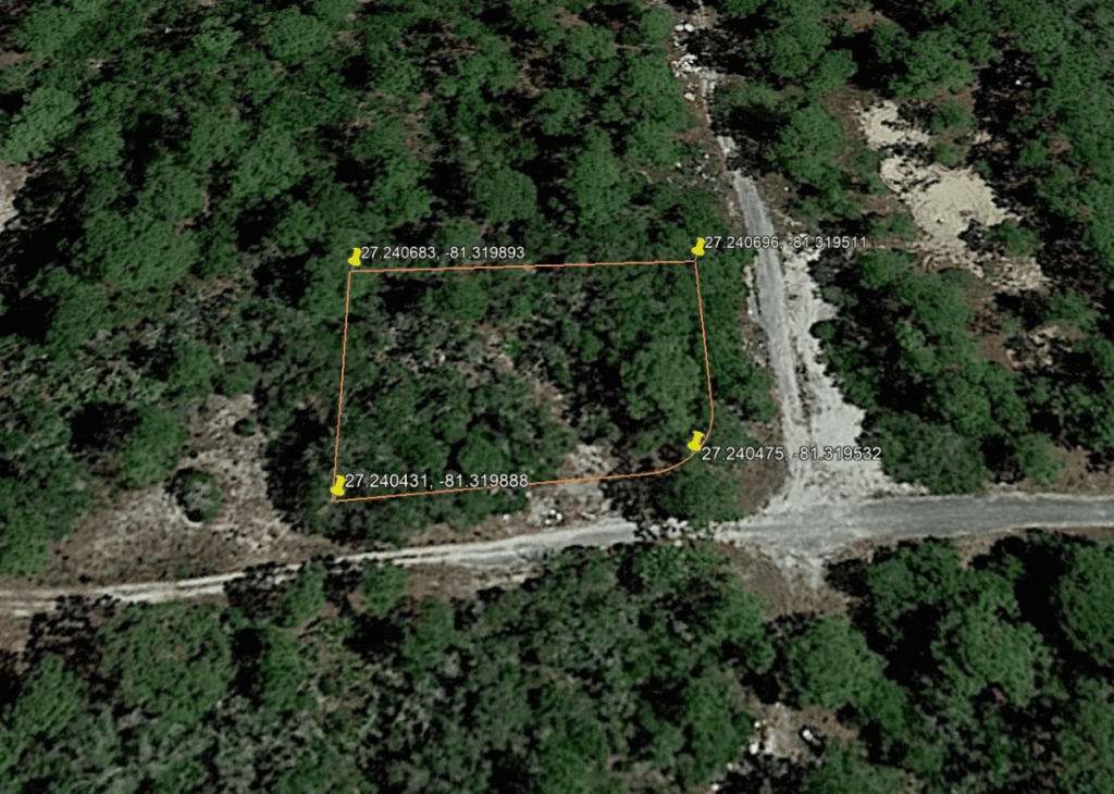 Aerial view of a forested area with an orange property boundary and yellow corner pins, showing GPS coordinates along the edges.