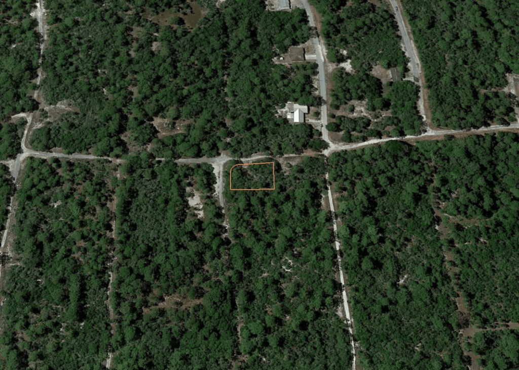 Aerial view of a wooded area with a small rectangular parcel outlined in orange near a road and a few buildings nearby.
