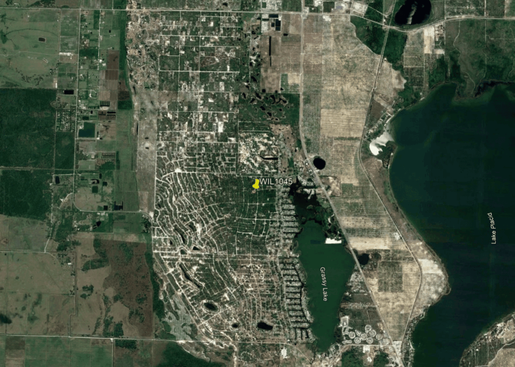 Satellite view of a suburban area around Grassy Lake with a dense grid of streets, bordered by water to the east and agricultural fields to the west; a yellow marker labeled WIL1045 appears near the center.