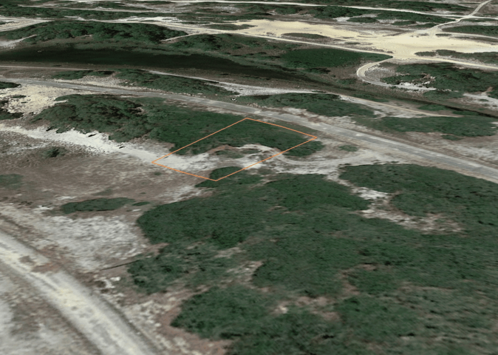 Aerial view of barren land with a rotated orange rectangle marking a plot beside a dirt road and patches of scrubby vegetation.