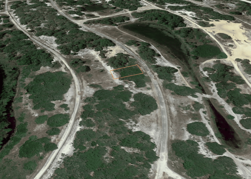 Aerial view of a rural, wooded area with a small rectangular plot outlined in orange beside a curved road.