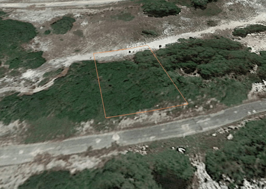 Aerial view showing a dirt road and scrubby hillside with an orange polygon outlining a rectangular land parcel among shrubs.