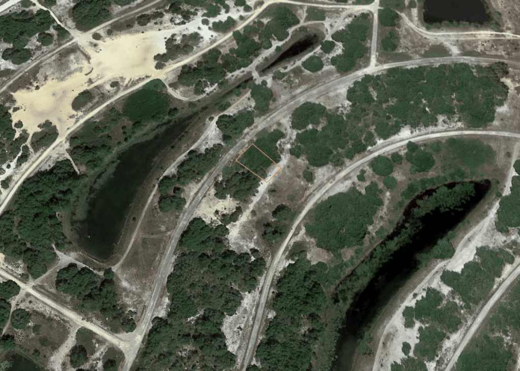 Aerial view of a winding road through a scrubby, hilly landscape; an orange outlined parcel sits near the center.