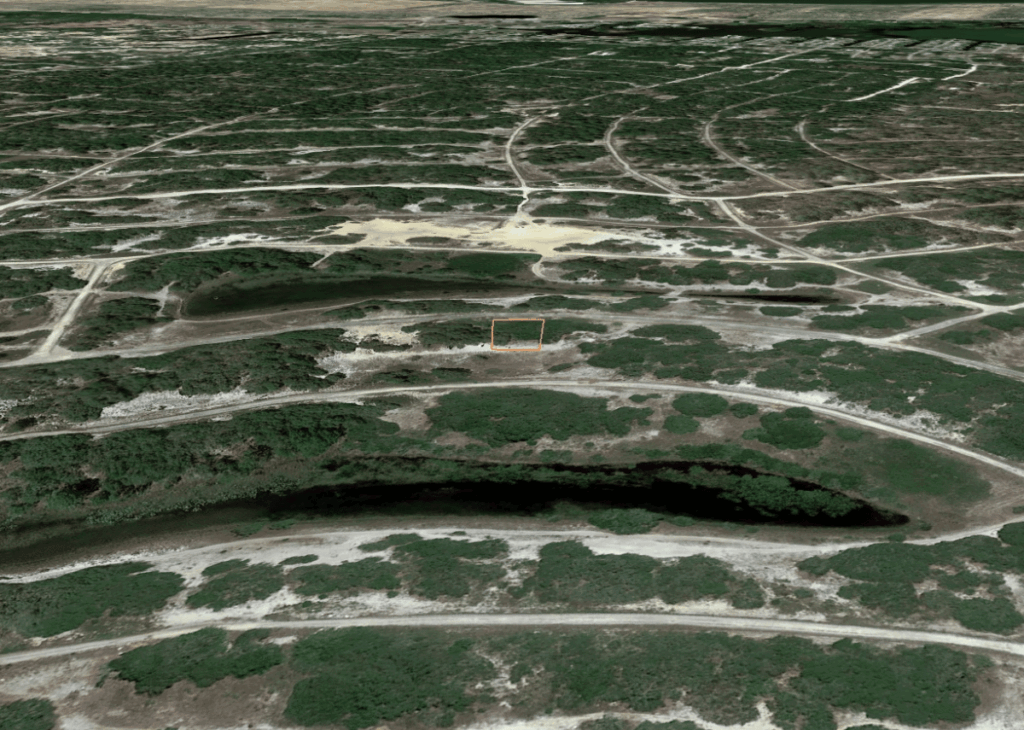 Aerial view of a barren, scrubby landscape with a grid of dirt roads; an orange rectangle marks a small cleared patch.