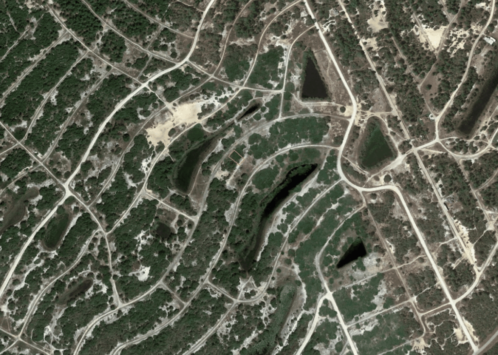 Aerial view of a hill country with winding dirt roads and several empty quarry pits amid sparse vegetation.