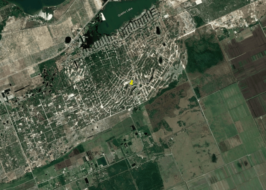 Satellite view of a town with a dense grid of streets near Grassy Lake; surrounding farmland to the east and south, with a yellow marker labeled WIL1072 in the center.
