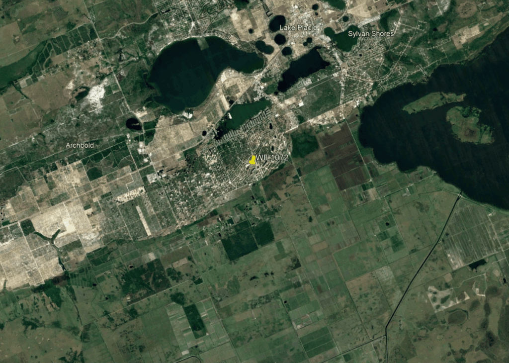 Aerial view of a town near a large lake with the label WIL1072 marked on a yellow pin, surrounded by agricultural fields and green areas.