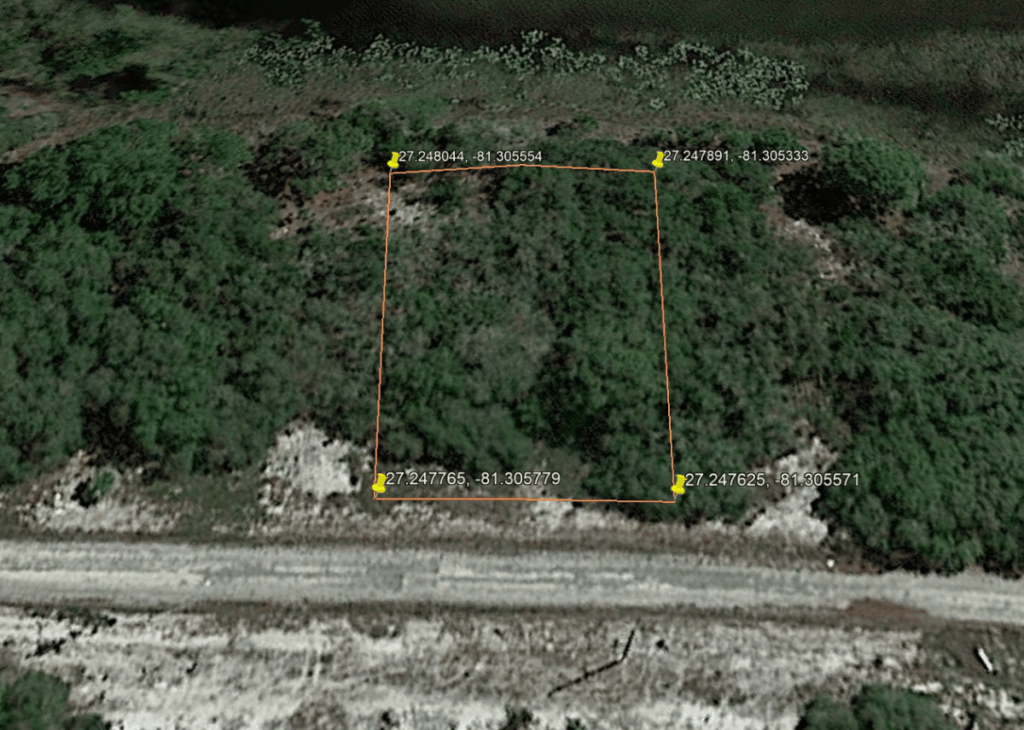 Aerial view of a wooded lot outlined by an orange square boundary with yellow corner markers and GPS coordinates at each corner along a dirt road edge.